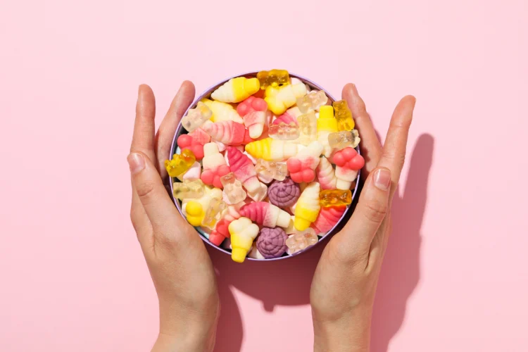jelly-candies-in-box-and-female-hands-on-pink-back-2023-11-27-05-29-29-utc